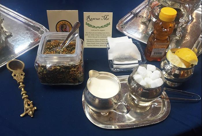 Metal trays with jars and containers holding tea leaves, honey, lemon, milk, and sugar cubes