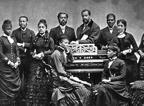 Group of Black singers gathered around an organ
